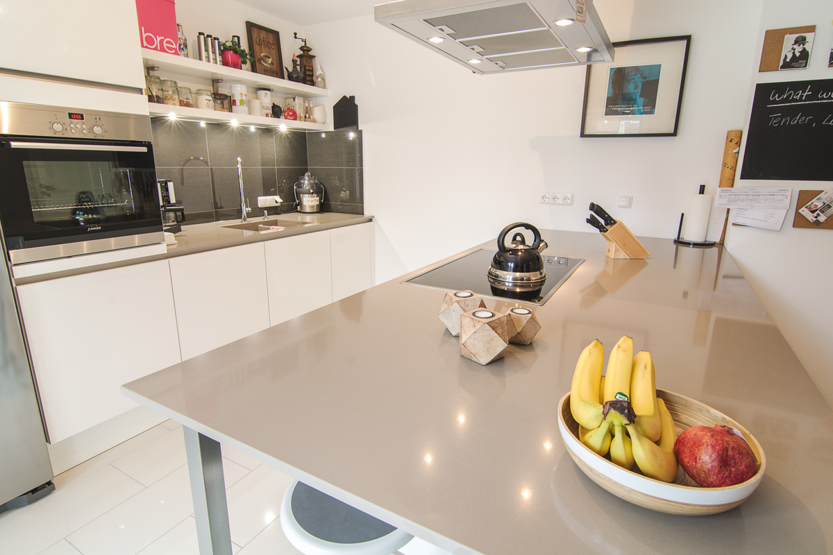 Weiße Designerküche mit grauer Arbeitsplatte und hochwertigen Elektrogeräten mit Obstschale, Fotos aus der Galerie