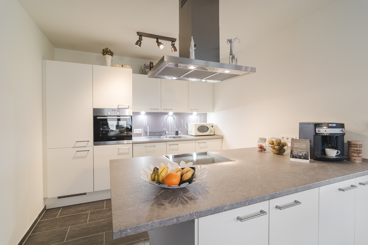 Weiße Designerküche mit grauer Arbeitsplatte und hochwertigen Elektrogeräten, Galerie