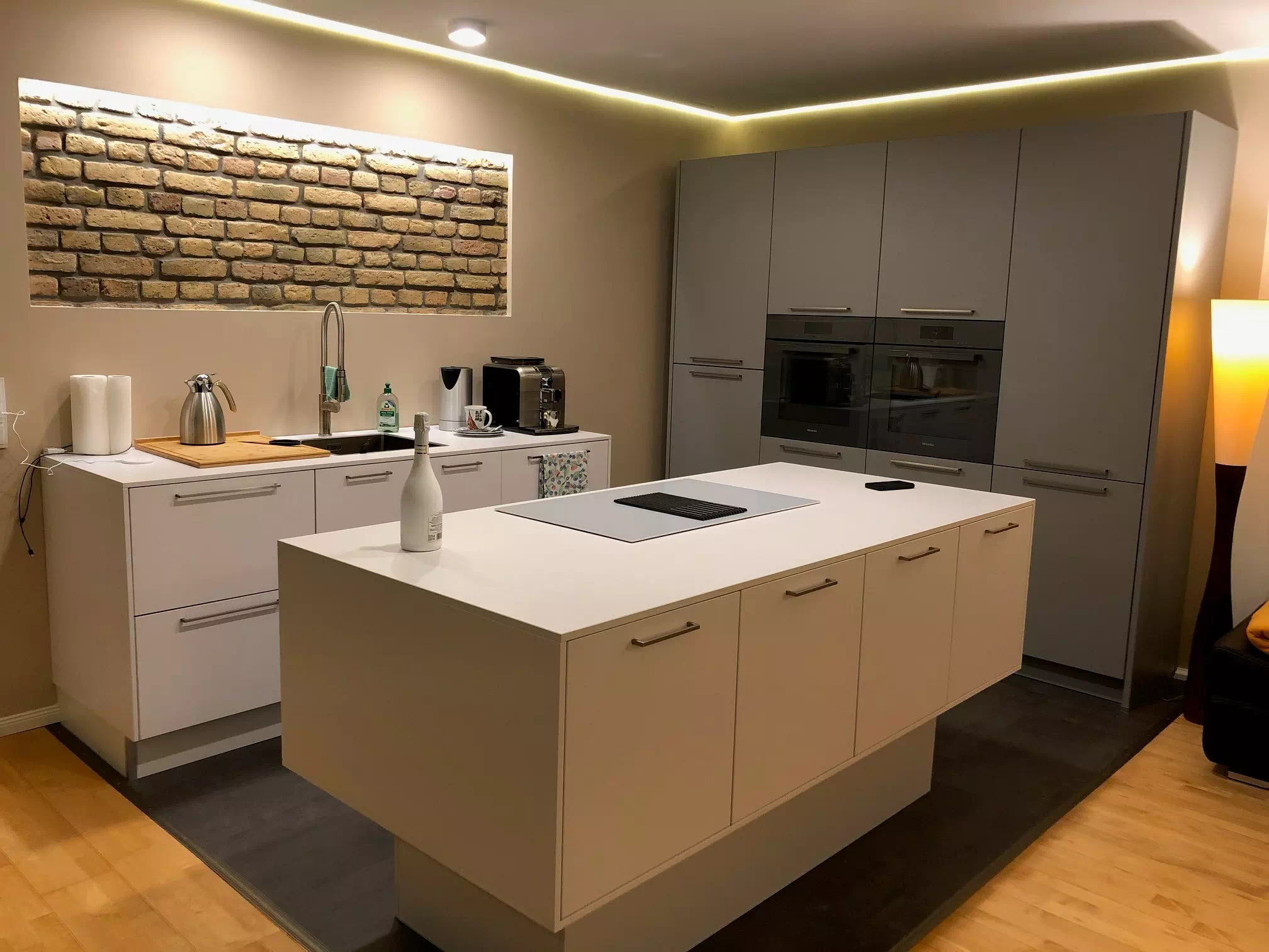 Weiße, moderne Kücheninsel mit grauer Küchenrückwand, in warmen Licht
