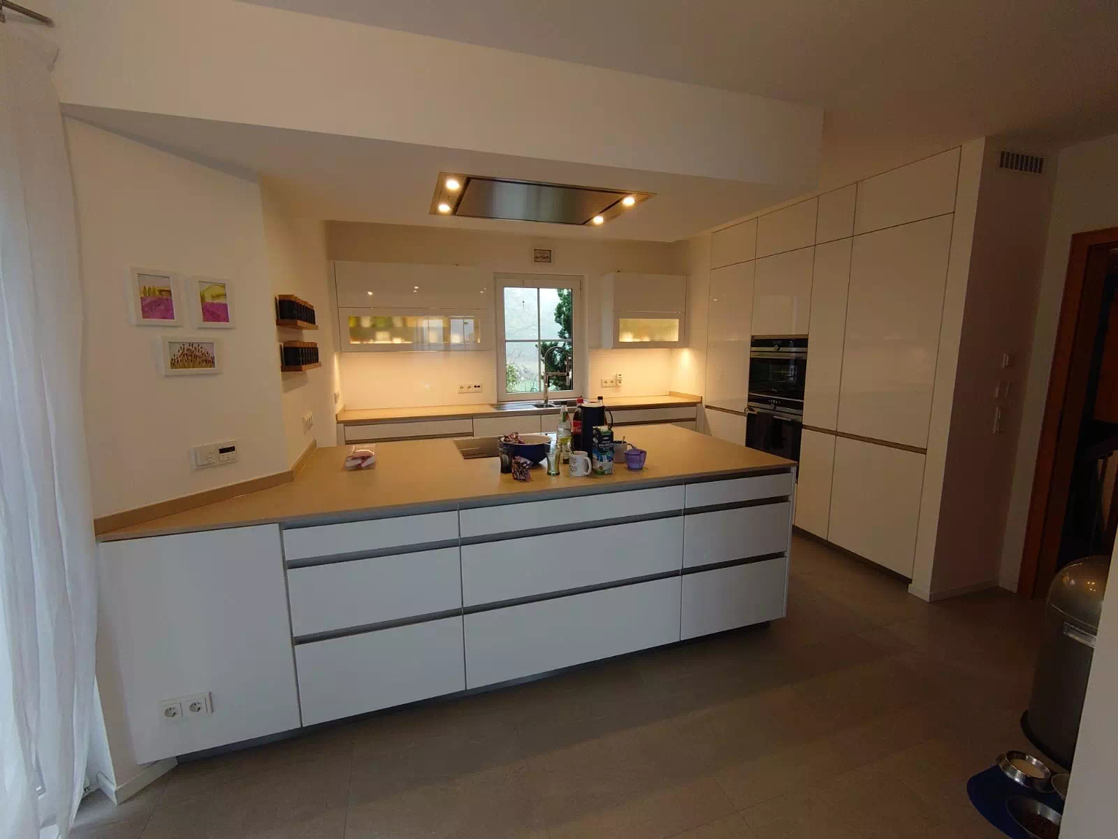 Moderne, weiße Küche mit hellbrauner Arbeitsplatte in wohligem, warmen Licht