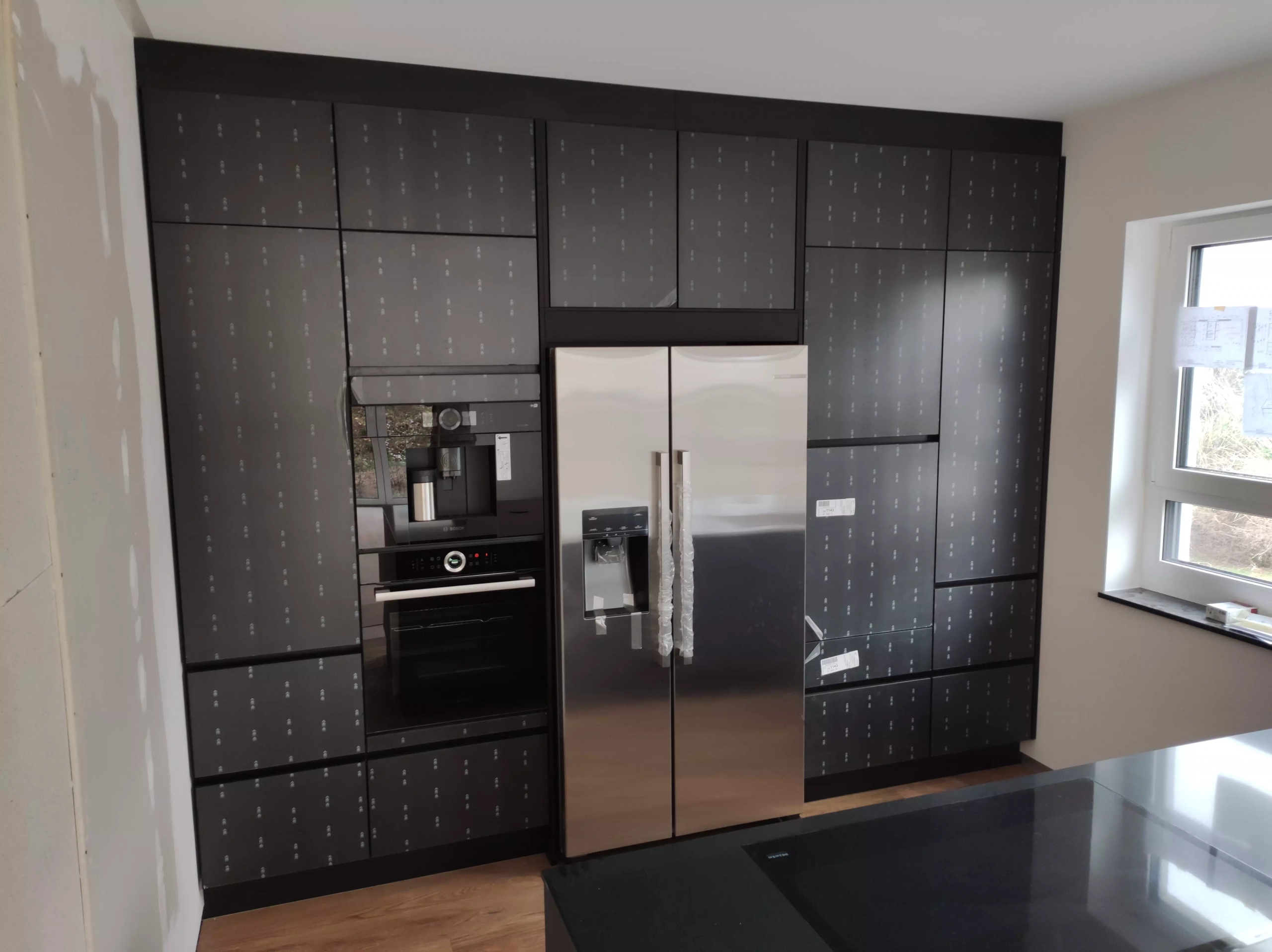 Moderne, schwarze Küchenrückwand mit Kühlschrank, Ofen und Kaffeemaschine, im Aufbauprozess